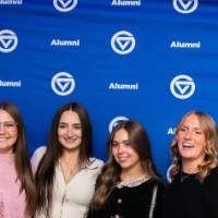 A large group of grads smile in front of GVSU Alumni backdrop